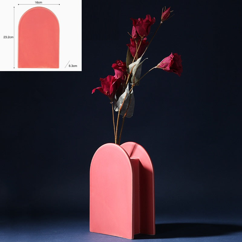 Pink vase with a minimalist design holding red flowers on a dark background