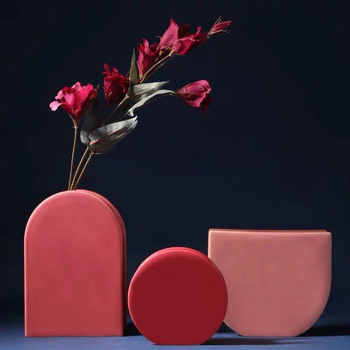 Three pink ceramic vases with a single red flower on a dark background
