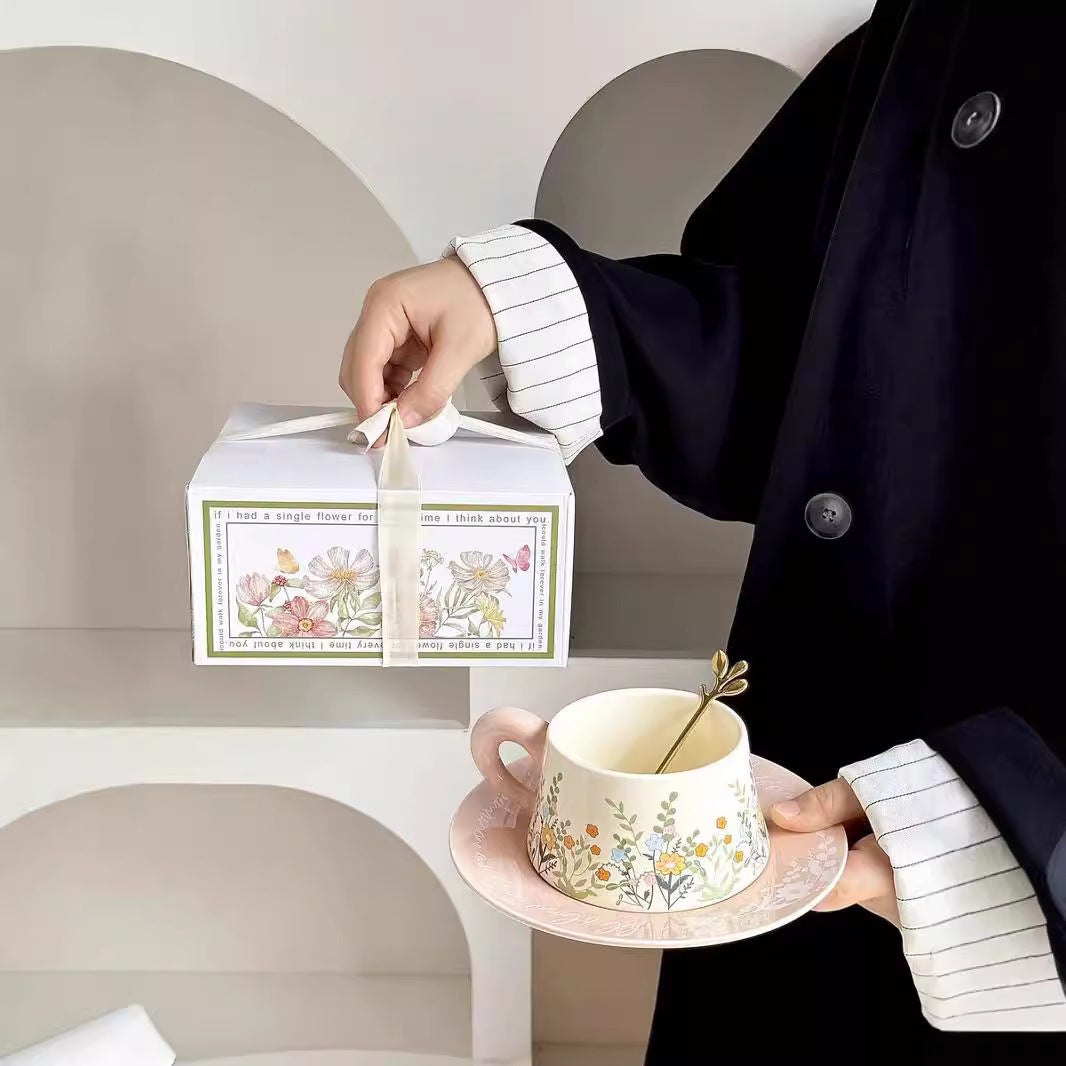 Person holding a floral teacup and saucer with a matching box on a neutral background
