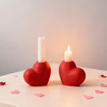 Two red heart-shaped candle holders with candles on a light surface with heart-shaped confetti.