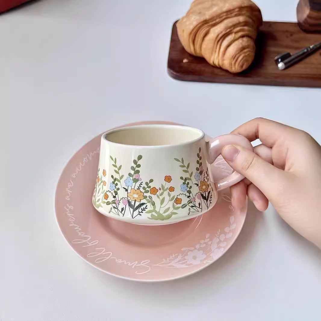 Hand holding a floral-patterned mug with a matching saucer on a light surface.
