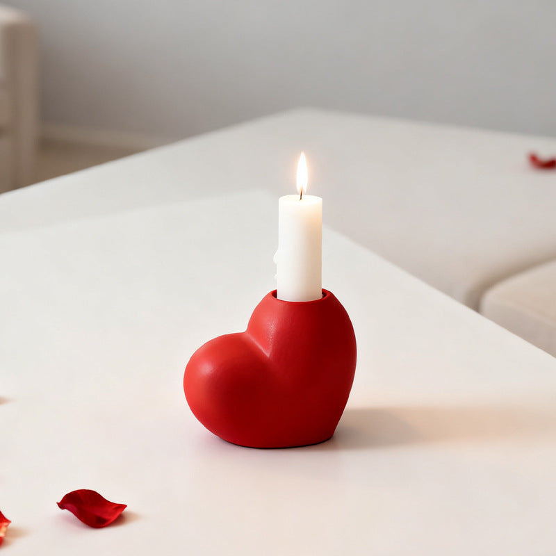 Red heart-shaped candle holder with a lit white candle on a light surface.