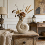 Decorative vase with dried flowers on a wooden table in a room with a lamp and wall art.
