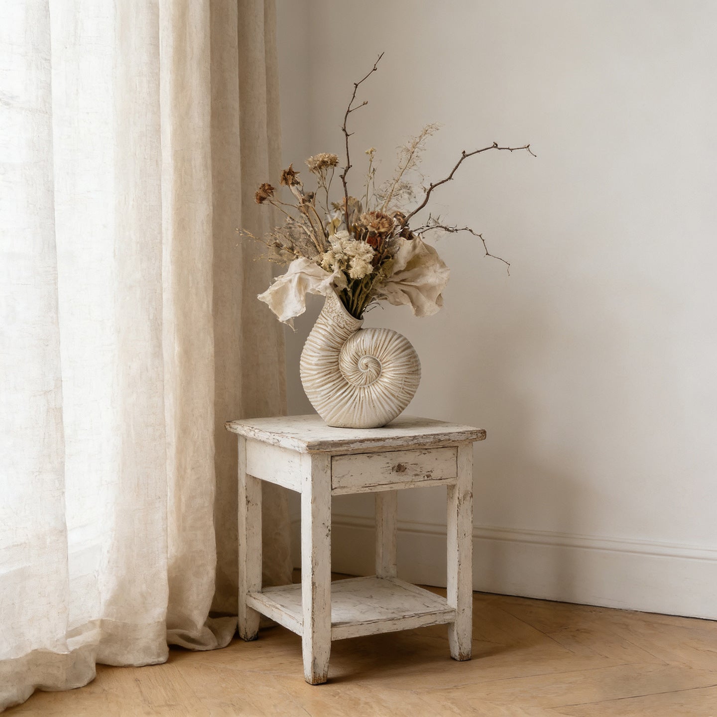 Decorative vase with dried flowers on a wooden side table against a neutral wall.