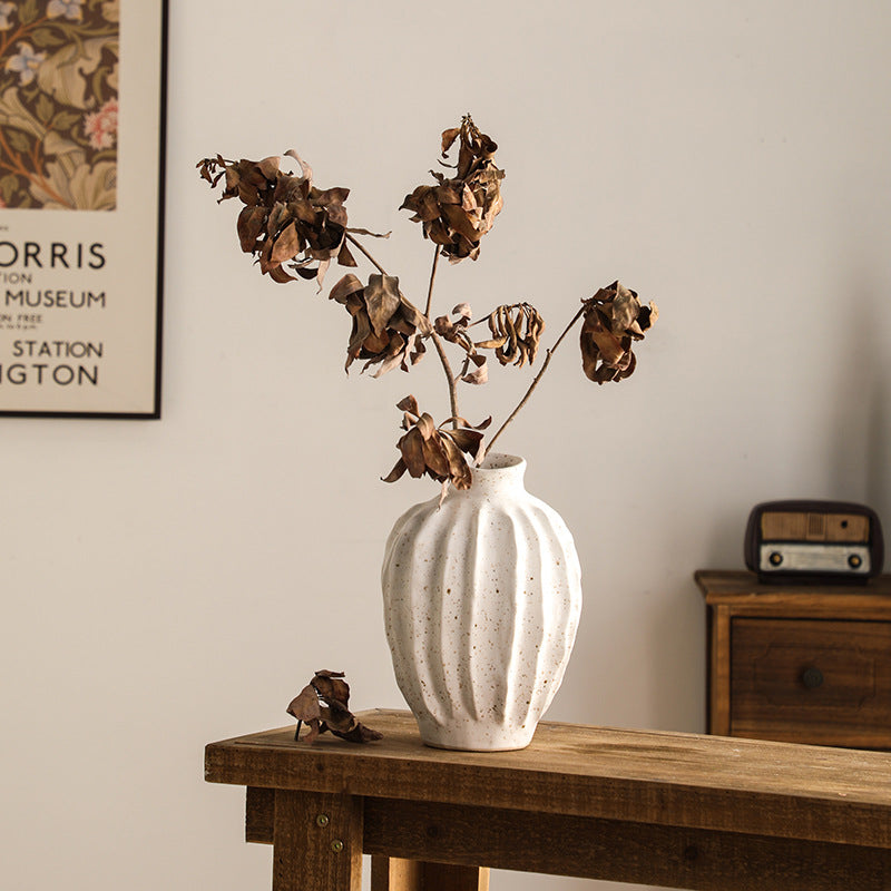White textured vase with dried flowers on a wooden table against a neutral wall.
