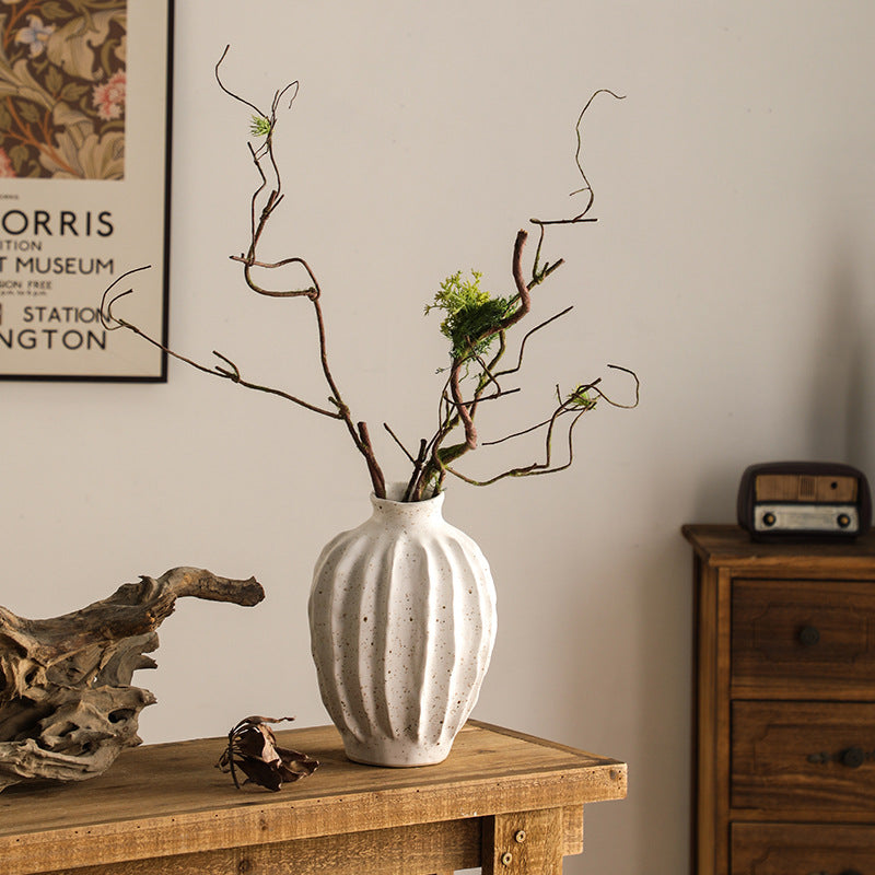 White textured vase with branches on a wooden table against a neutral wall.